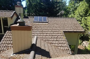 Photo of a roofer on the roof hammering roof tiles.