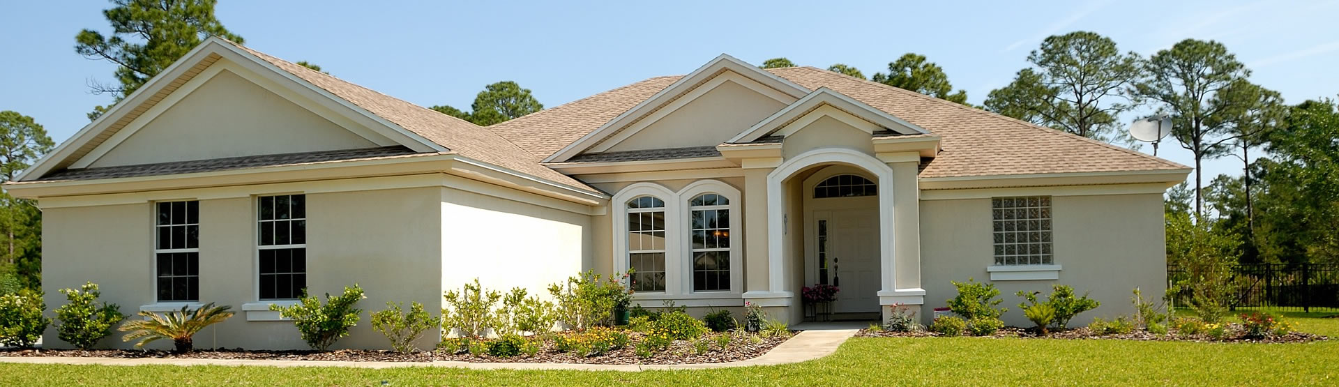 A nice one-story light yellow home with nice green lawn and landscaping in the front yard.